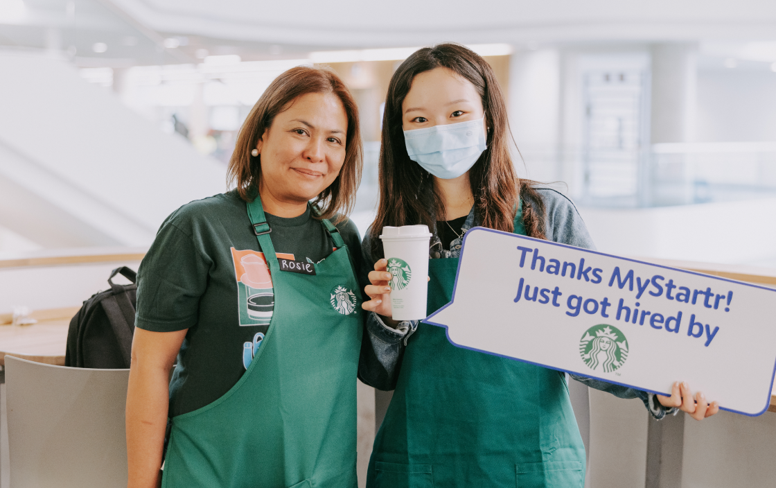 Young employee holding sign thanking MyStartr for helping get a job at Starbucks